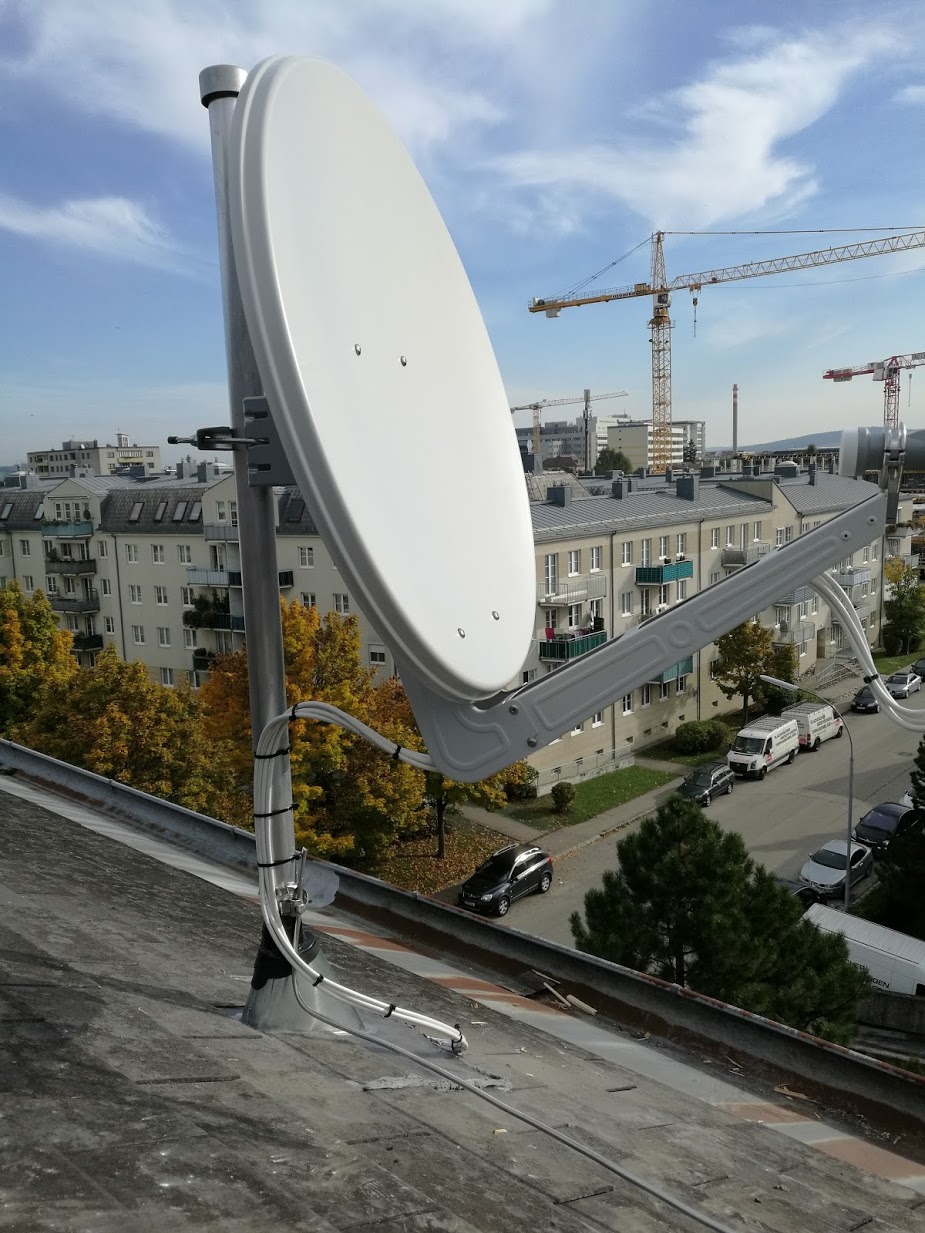 Satellitenschüssel an Hausdach montiert, fachmännisch ausgemessen und eingerichtet, blauer Himmel und Baukran im Hintergrund